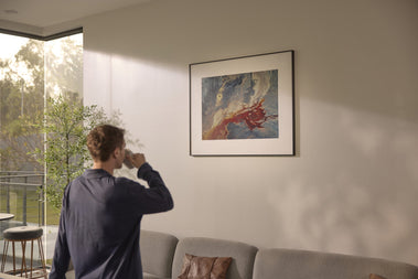 A man in a navy blue shirt stands in a modern living room, looking at a framed abstract art on InkPoster