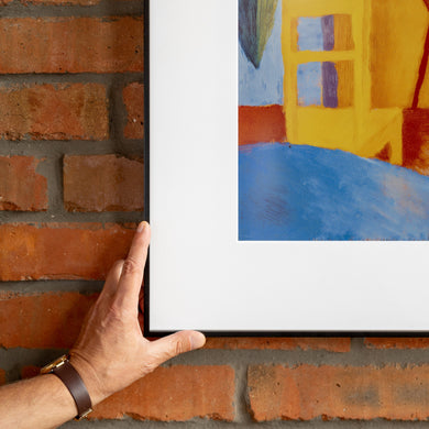 Hand adjusting InkPoster e-paper art frame on a red brick wall close-up