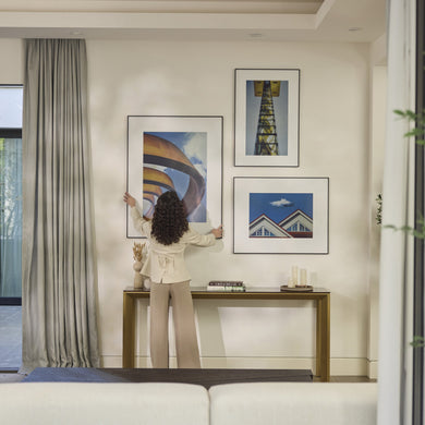 Woman arranging three InkPoster digital art frames on a modern living room gallery wall
